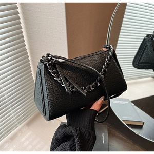 Detail of black lychee grain leather handbag with chunky metal chain and slim strap