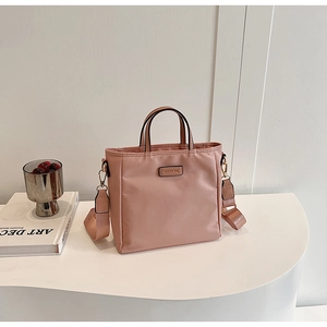 Détail du sac seau en nylon rose poudré avec bandoulière large sur socle blanc