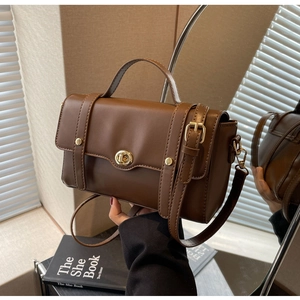 Détail d'un sac bandoulière en cuir marron avec fermoir tournant doré et poignée supérieure