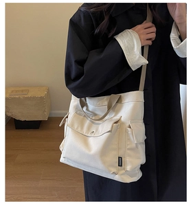 Detailed view of cream canvas tote bag with multi-pocket design and wide shoulder strap