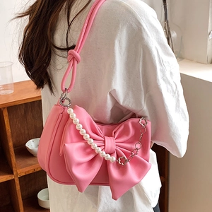 Pink bow shoulder bag with pearl chain and metal flower charm in a lifestyle setting