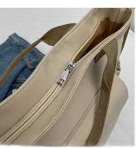 Detail of smooth metal zipper closure on durable beige canvas tote bag with brown handles
