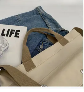 Detail of beige canvas tote bag showing brown webbing handles and metal button closure