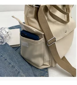 Detail of beige canvas shoulder bag featuring a functional side pocket for mobile phones
