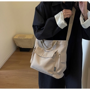 Detail of beige canvas tote bag with front flap pocket and adjustable shoulder straps