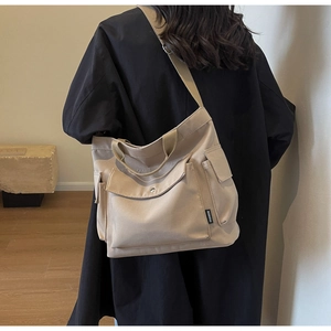 Detail of beige canvas tote bag with flap pocket and side woven label on back-view model