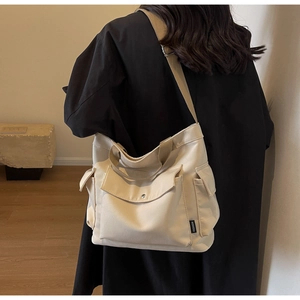 Detail view of off-white canvas tote bag featuring functional external pockets and wide strap