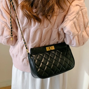 Quilted black crossbody bag with gold chain strap worn with pink sweater and white skirt