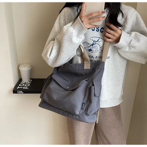 Detailed view of gray canvas tote bag with wide strap and fashion tag on side pocket