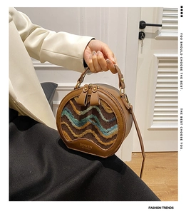 Detail of round crossbody bag with brown leather trim and colorful wavy fabric texture