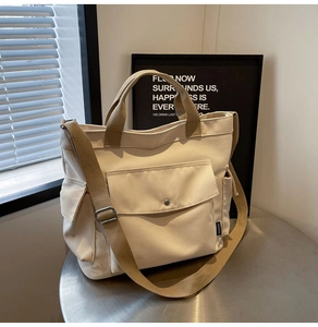 Detail of beige canvas tote bag showing front flap pocket and adjustable strap on a table
