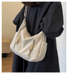 Détail d'un grand cabas en toile beige avec zips métalliques porté par un mannequin en manteau