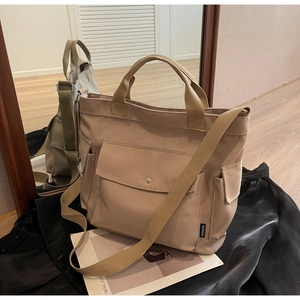 Detail of khaki canvas tote bag featuring functional front pockets and a fashion logo label