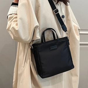Sac seau en nylon noir avec large bandoulière et détails dorés porté par un modèle