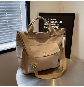 Detail of beige canvas tote bag with metal button pocket and black brand label