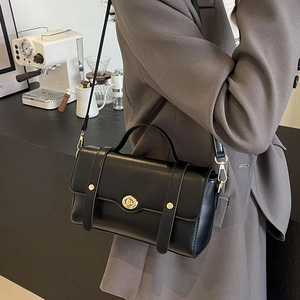 Sac bandoulière en cuir noir avec fermoir doré porté par un mannequin dans un café