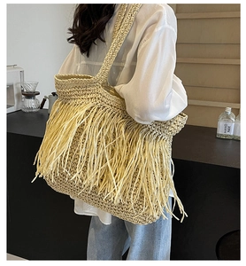 Detail of beige straw shoulder bag featuring decorative long tassels and woven texture