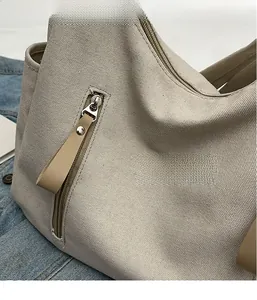Détail de la texture du sac en toile, fermeture éclair argentée et tirette en cuir beige
