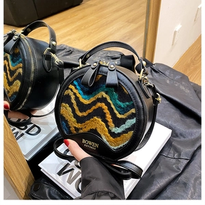 Detail of round crossbody bag featuring wavy patterned tweed and dual gold metal zippers