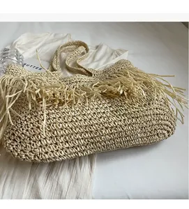 Detail of a large beige straw woven tote bag with tassels on soft fabric background