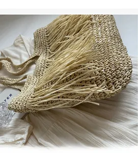 Detail of bohemian straw woven tote bag with long fringe tassels on white fabric