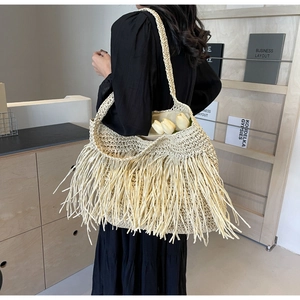 Detail of a large cream woven straw shoulder bag with long fringe tassels and inner lining