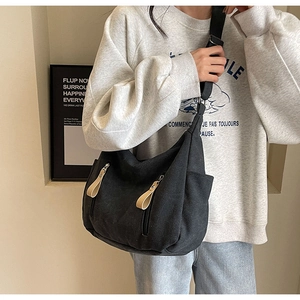 Détail du sac hobo en toile noire avec plusieurs poches zippées et tirettes décoratives