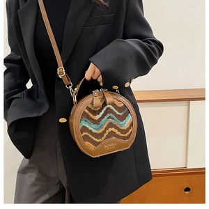 Detail of vintage round crossbody bag in brown leather and patterned fabric held by a model