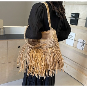 Close-up of handmade straw tote bag featuring long decorative tassels and woven texture