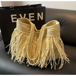 Detail of a large beige straw tote bag with long dense fringe on a black sofa background