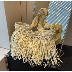 Close-up of beige woven straw tote bag with long fringe details for beach vacations
