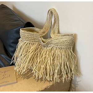 Close-up of beige woven straw tote bag with long decorative fringe and textured details