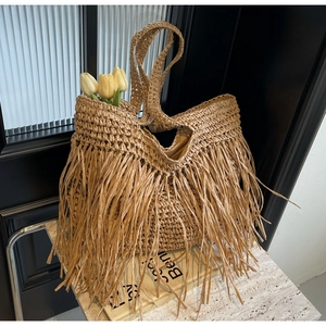 Detail of bohemian straw woven tote bag featuring long tassels and rustic texture