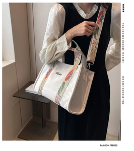 Close-up of white canvas tote bag with vibrant floral embroidery on wide shoulder strap