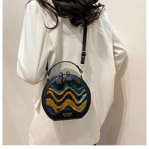Detail of the round crossbody bag showing textured wavy pattern and black leather trim