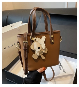 Close-up of brown leather bucket bag with adjustable strap and designer bear charm
