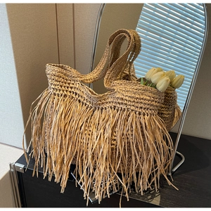 Detailed macro view of woven straw tote bag featuring long decorative fringe and tulips