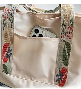 Detail of canvas tote bag back pocket holding a smartphone with floral embroidered handles