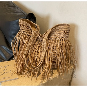 Detailed view of handmade straw tote bag featuring dense fringe accents and woven handles