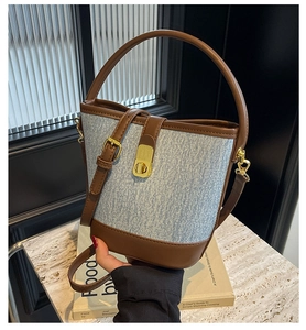 Detail of blue denim texture and brown leather trim on the bucket bag with gold clasp