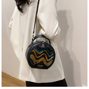 Close-up of black round bag featuring colorful wave embroidery and gold logo detail