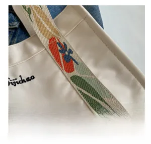 Close-up of durable canvas tote bag seams and colorful embroidered floral shoulder strap