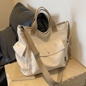 Retro multi-pocket canvas tote bag in off-white with brown straps on a stone base