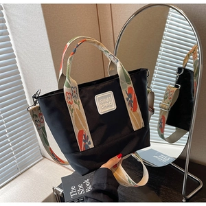 Detailed close-up of a black canvas tote bag with floral straps and rubber logo patch