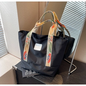 Detail of black nylon tote bag with colorful printed strap and minimalist logo patch