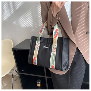 Detail of a large black canvas tote bag featuring colorful floral jacquard wide straps