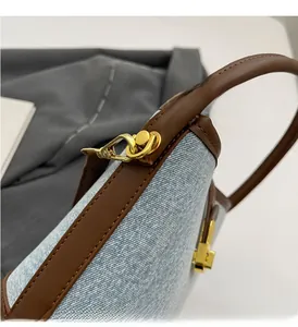 Detailed close-up of light blue denim bucket bag with brown leather trim and gold hardware