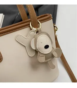 Detail of a beige tote bag with a cartoon monkey leather charm and Y-shaped pendant