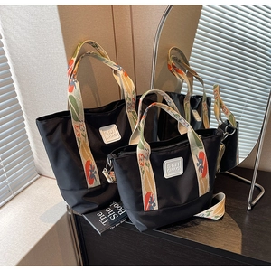 Detail of black tote bag set with floral straps on a wooden surface with mirror reflection