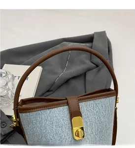 Detail of denim bucket bag showing brown leather handle and gold metal press lock